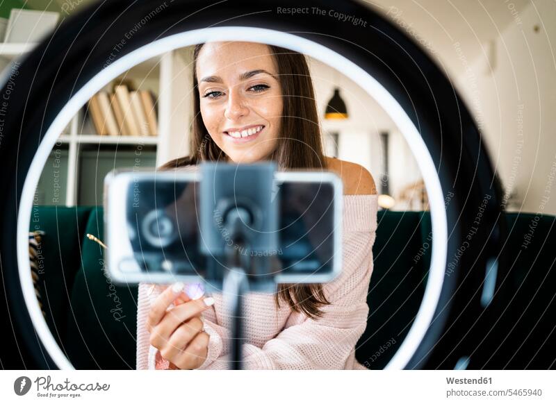 Smiling young female influencer vlogging through smart phone at home color image colour image indoors indoor shot indoor shots interior interior view Interiors
