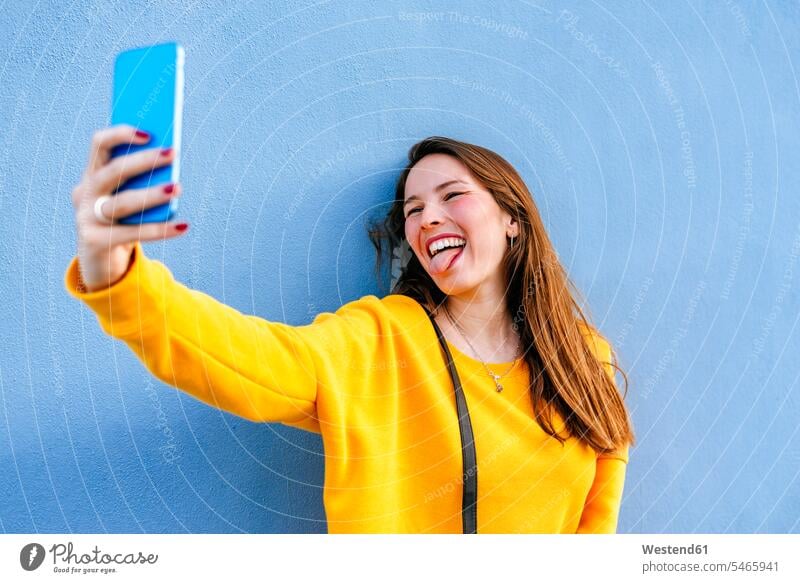 Happy young woman taking a selfie at a wall sticking out tongue females women Selfie Selfies tongues walls Adults grown-ups grownups adult people persons