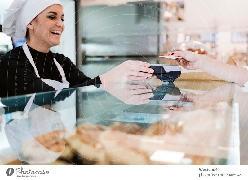 Happy baker receiving contactless payment through credit card from customer at bakery color image colour image indoors indoor shot indoor shots interior