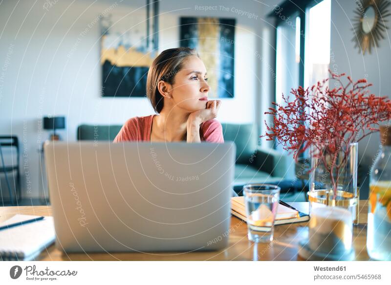 Thoughtful young woman with laptop on desk looking away while sitting at home color image colour image indoors indoor shot indoor shots interior interior view