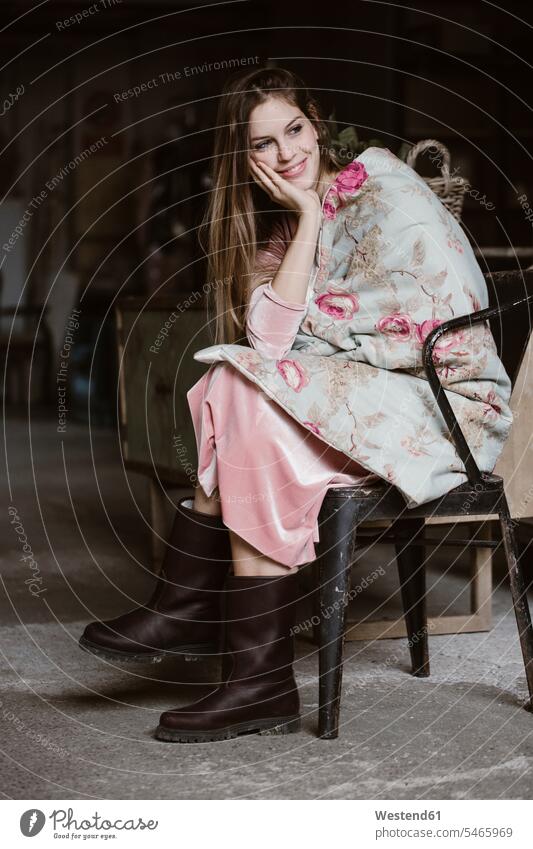 Portrait of smiling young woman sitting in a loft wrapped in blanket with floral design lofts floral pattern Flowered Floral Print Floral Motif portrait