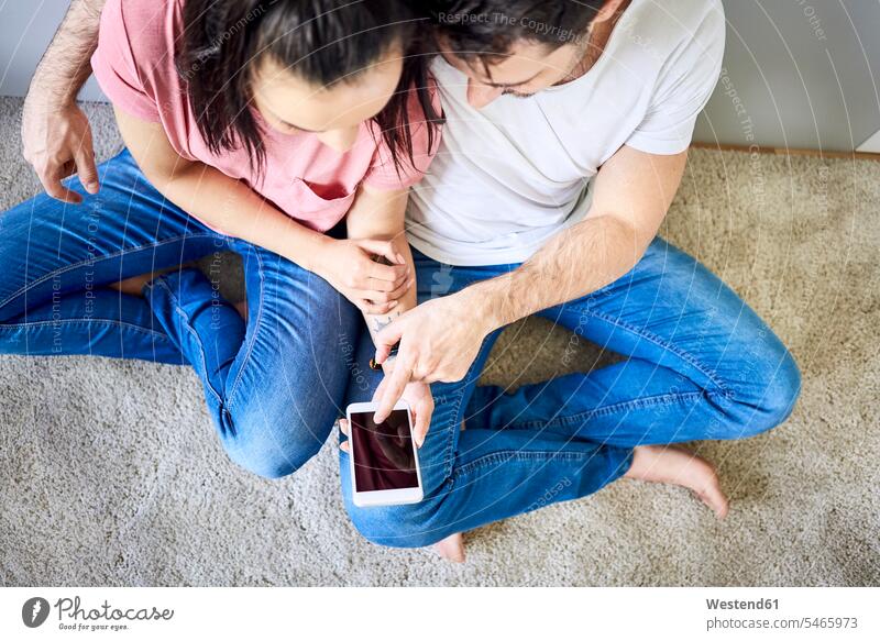 Couple using smartphone together sitting Seated couple twosomes partnership couples floor floors Smartphone iPhone Smartphones people persons human being humans
