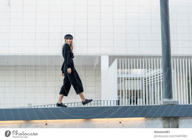 Young blond businesswoman wearing black sailor's cap and walking on a wall business life business world business person businesspeople business woman
