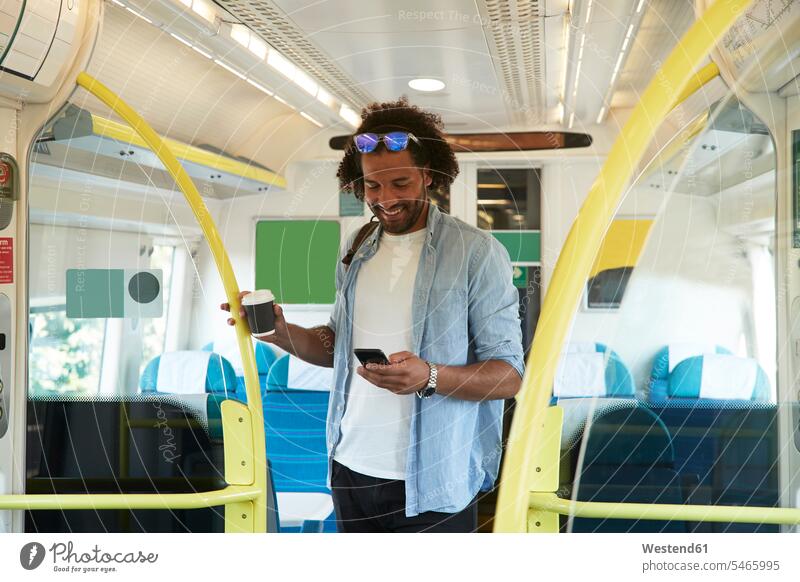 Young trendy man smiling while using smart phone in train color image colour image Vehicle Interior Train Interior railway railroad Railways railroads