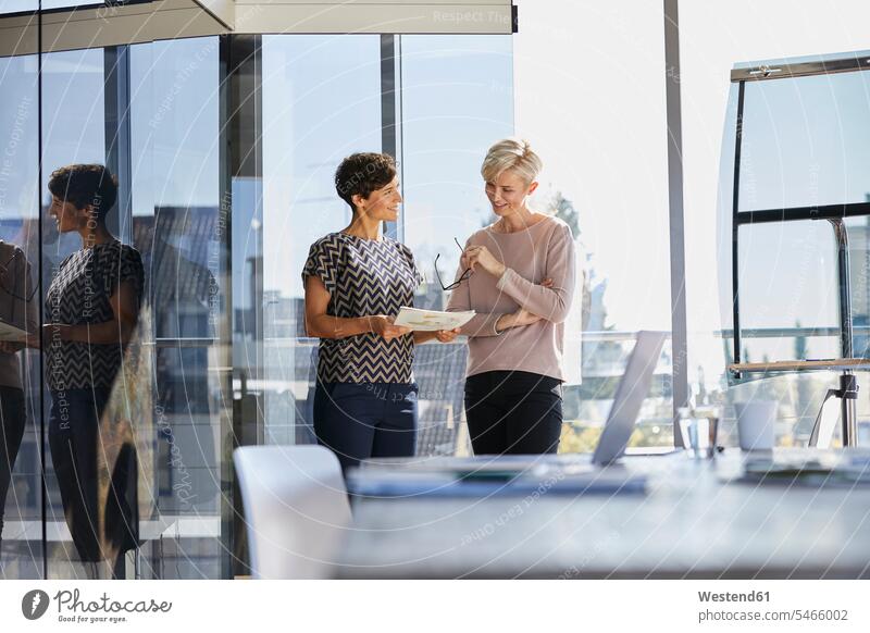 Two smiling businesswomen discussing document at the window in office businesswoman business woman business women offices office room office rooms windows
