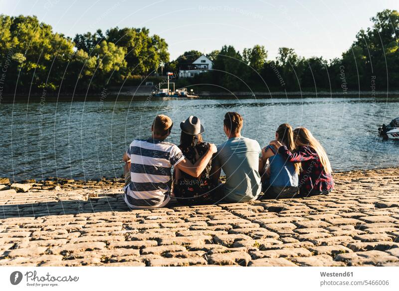 Group of friends sitting at the water looking out Seated mate group of people groups of people embracing embrace Embracement hug hugging friendship persons
