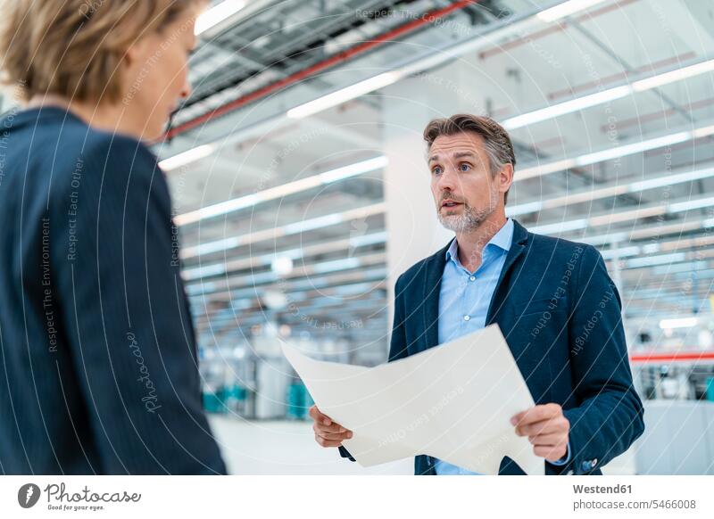 Businessman and businesswoman discussing plan in a factory hall human human being human beings humans person persons caucasian appearance caucasian ethnicity