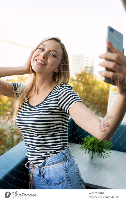 Smiling young woman taking a selfie on balcony Selfie Selfies balconies mobile phone mobiles mobile phones Cellphone cell phone cell phones smiling smile