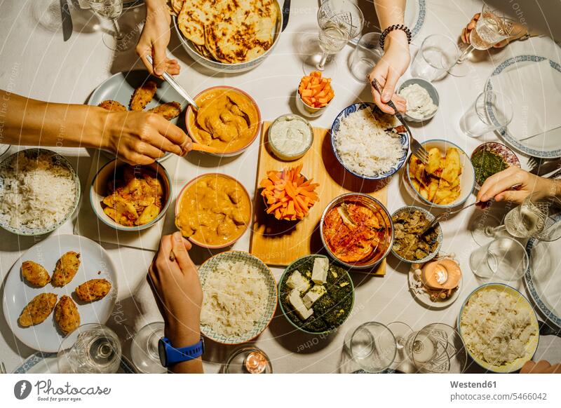 Hands of people dining together around table set with Indian food indoors indoor shot indoor shots interior interior view Interiors overhead view directly above
