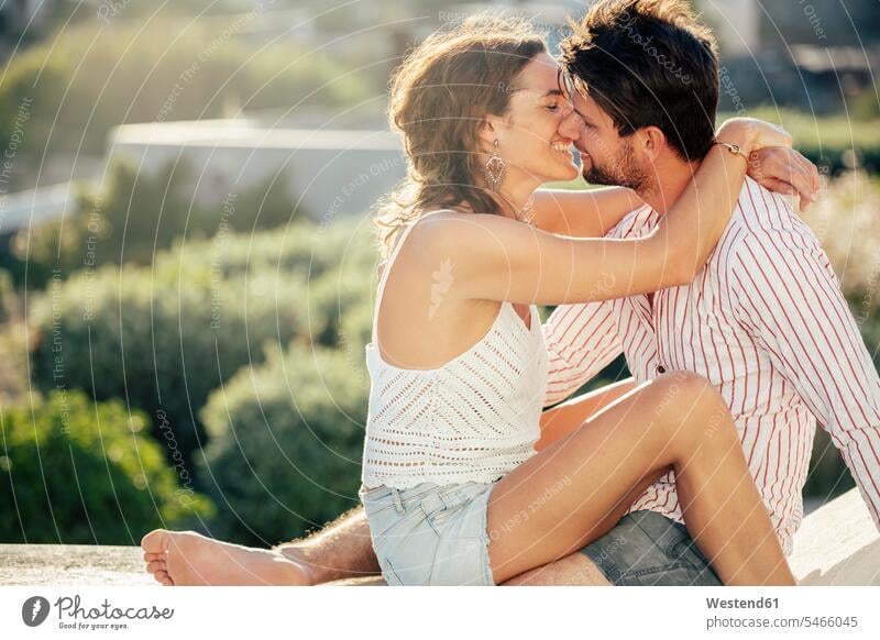 Romantic couple sitting on wall, embracing, enjoying holidays kiss kisses smile Seated embrace Embracement hug hugging seasons summer time summertime summery