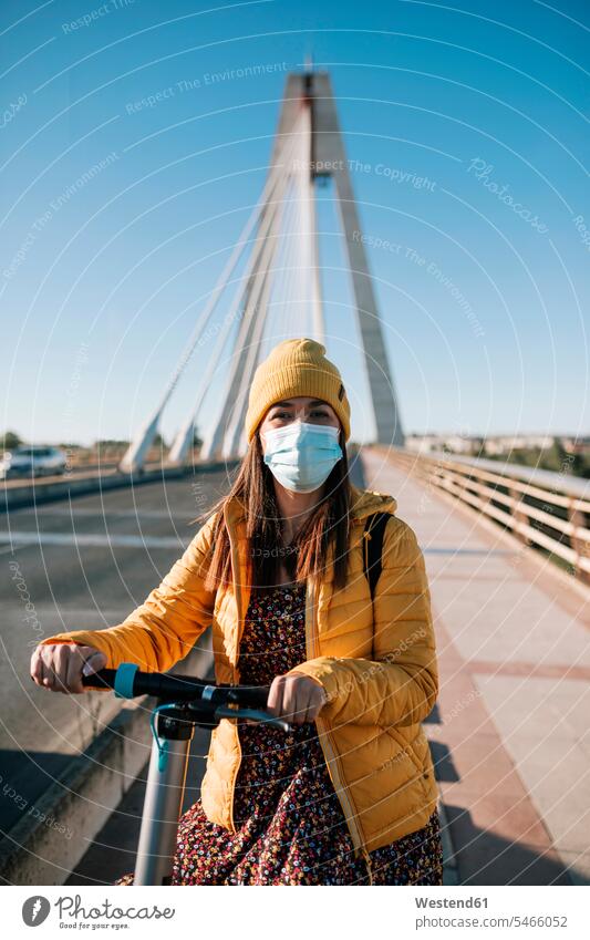 Woman in protective face mask with electric scooter on bridge in city during COVID-19 color image colour image outdoors location shots outdoor shot