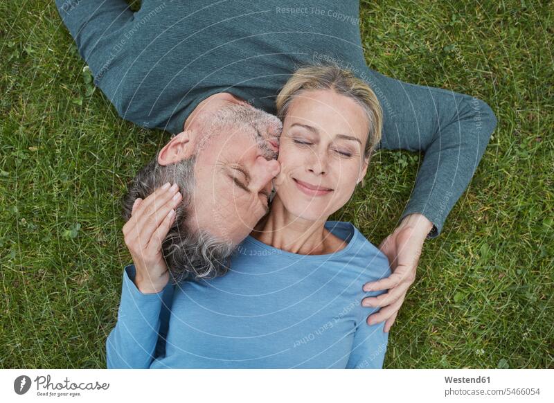 Top view of affectionate mature couple lying in grass jumper sweater Sweaters touch cuddle snuggle snuggling kiss kisses smile relax relaxing relaxation delight