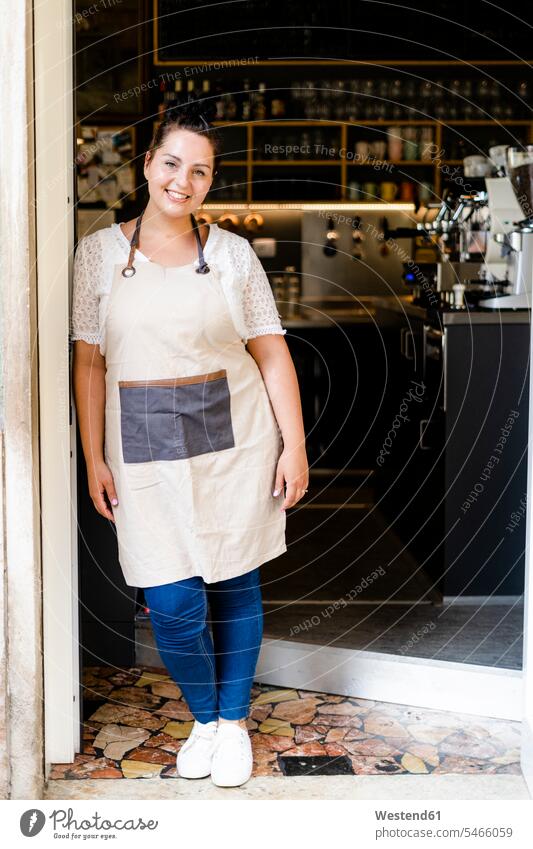 Smiling female owner standing by glass door at entrance of coffee shop color image colour image Millennials Millennial Generation young adults Adults grownup