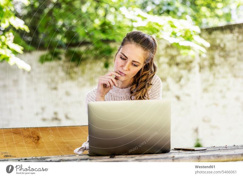 Portrait of pensive woman sitting on bench at courtyard looking at laptop benches portrait portraits thoughtful Reflective contemplative courtyards courts