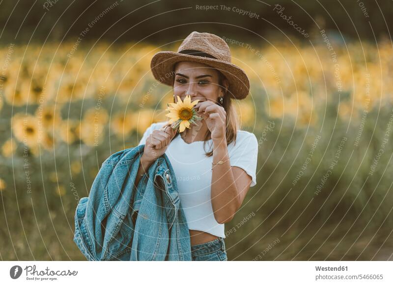 Portrait of young woman with blue denim jacket and hat in a field of sunflowers hats smile in the evening delight enjoyment Pleasant pleasure indulgence