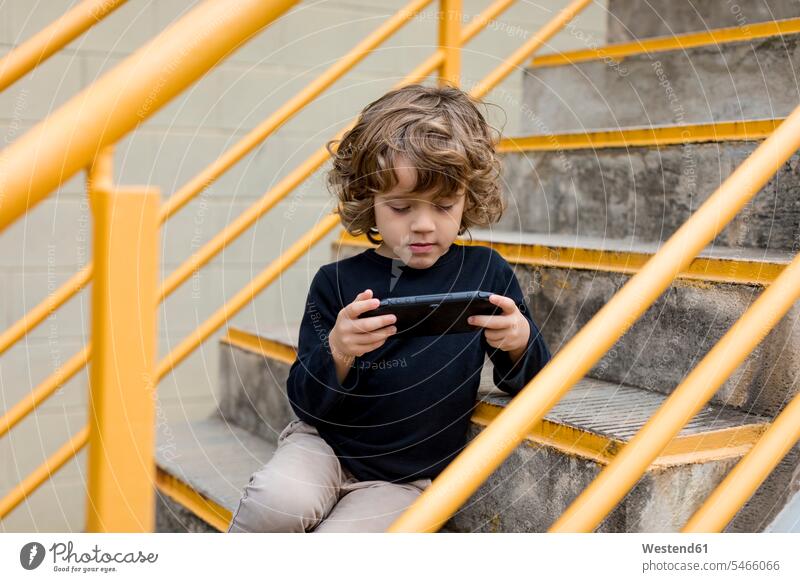 Boy sitting on stairs playing with handheld game console handhelds Seated Console stairway boy boys males child children kid kids people persons human being