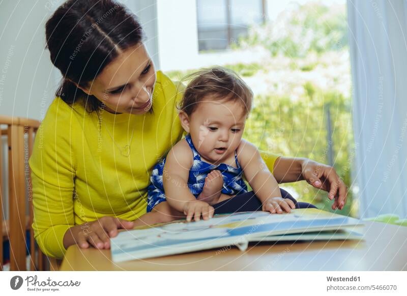 Mother and baby daughter looking at children’s book daughters eyeing infants nurselings babies mother mommy mothers ma mummy mama children's book