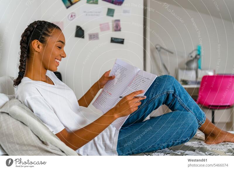 Teenage girl reading in exercise book sitting on bed at home color image colour image indoors indoor shot indoor shots interior interior view Interiors day