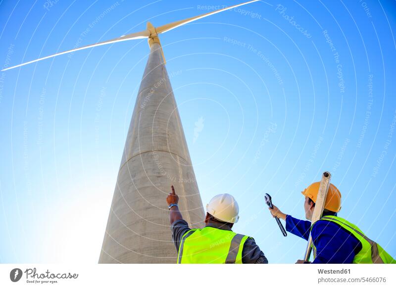 Low angle view of technicians in front of wind turbine wind turbines technology technologies engineering wind energy wind power renewable energy