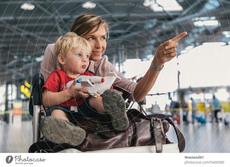 Germany, Cologne, portrait of mother and little son with baggage cart at airport terminal airports sons manchild manchildren mommy mothers mummy mama terminals