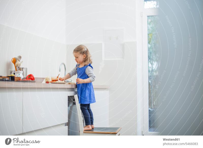 Girl eating food while standing on chair in kitchen at home color image colour image indoors indoor shot indoor shots interior interior view Interiors day