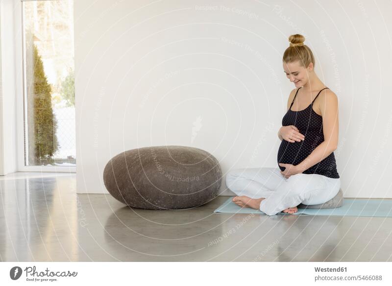 Smiling pregnant woman sitting on a yoga mat Pregnant Woman smiling smile Seated females women mindfulness aware awareness self-care relaxation exercise relaxed
