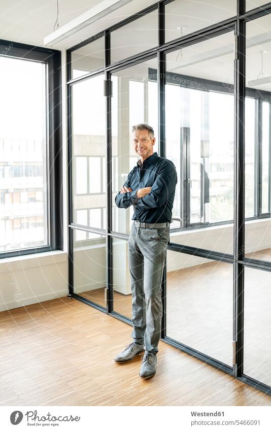 Businessman leaning on glass wall in his office, with arms crossed Occupation Work job jobs profession professional occupation business life business world