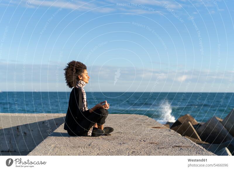 Woman sitting on wall in front of the sea meditating meditate Sea ocean woman females women walls Seated water Adults grown-ups grownups adult people persons