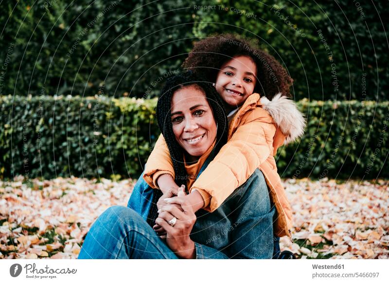 Smiling girl embracing mother from behind while sitting at park color image colour image outdoors location shots outdoor shot outdoor shots day daylight shot