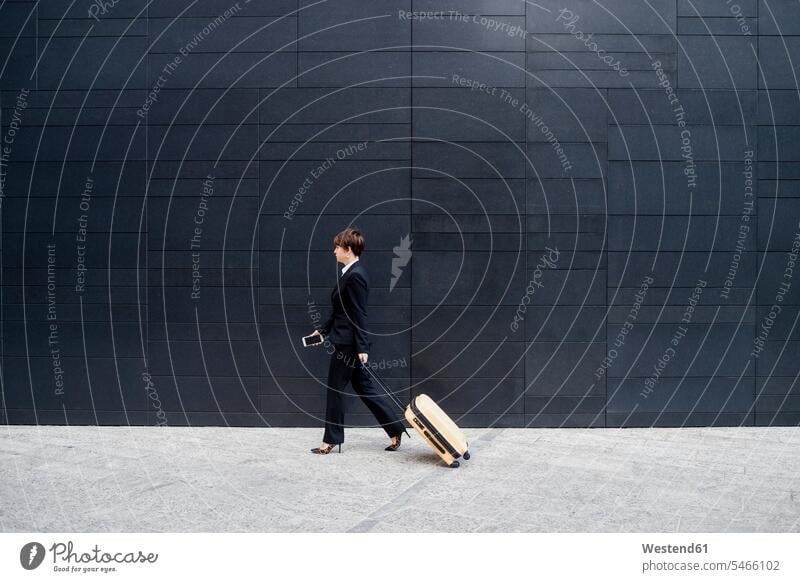 Businesswoman with suitcase walking on sidewalk by modern building in city color image colour image outdoors location shots outdoor shot outdoor shots day