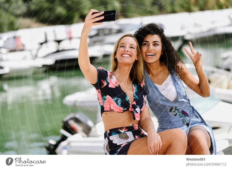 Two happy young women taking a selfie at marina in summer female friends mobile phone mobiles mobile phones Cellphone cell phone cell phones summer time summery