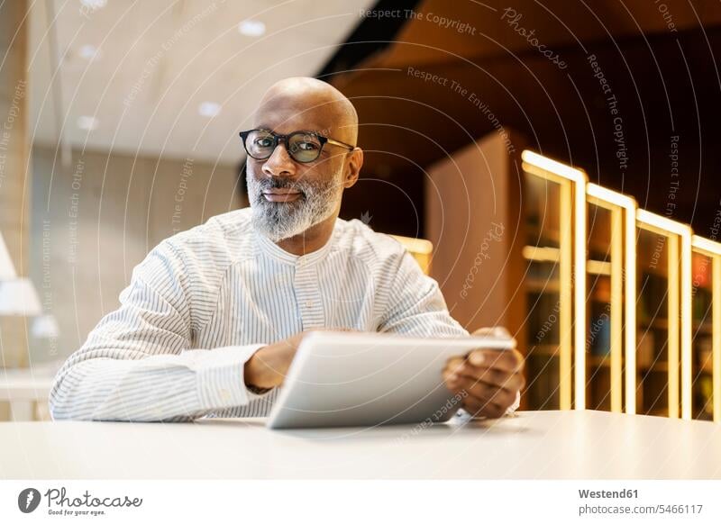 Portrait of mature man sitting at desk in a library with digital tablet Businessman Business man Businessmen Business men portrait portraits males digitizer