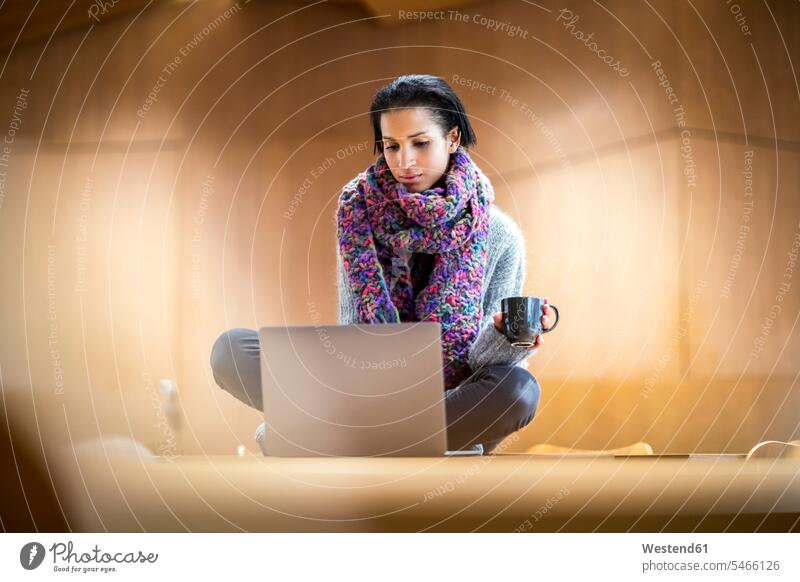 Portrait of fashionable young woman with cup of coffee sitting on conference table using laptop Laptop Computers laptops notebook use computer computers Germany