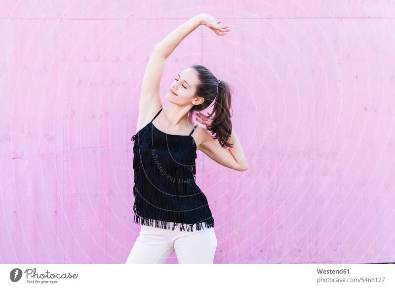 Smiling young woman stretching in front of pink wall smiling smile females women walls Rosy Adults grown-ups grownups adult people persons human being humans