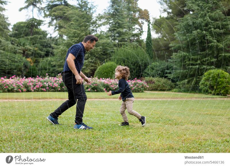 Father and son playing together in park father fathers daddy dads papa parks sons manchild manchildren parents family families people persons human being humans