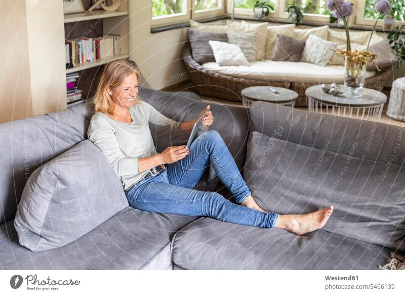 Laughing blond woman relaxing on couch at home using digital tablet human human being human beings humans person persons caucasian appearance