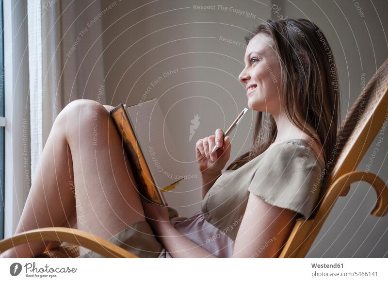 Smiling woman writing in daybook sitting on rocking chair diaries pencil pencils pens cogitate think smile write Writing - Activity Seated relax relaxing
