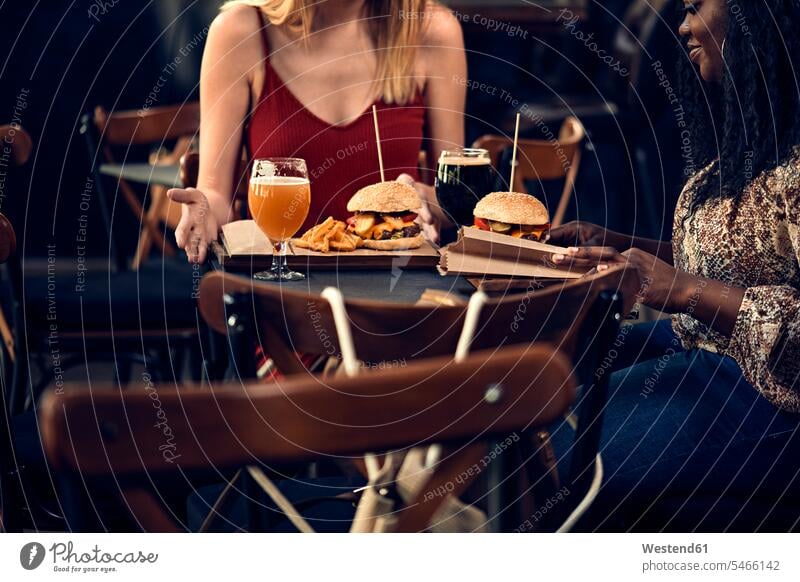 Female friends having a burger in a pub mate female friend Female Friendship Drinking Glass Drinking Glasses Beer Glasses Tables Seated sit relaxing free time