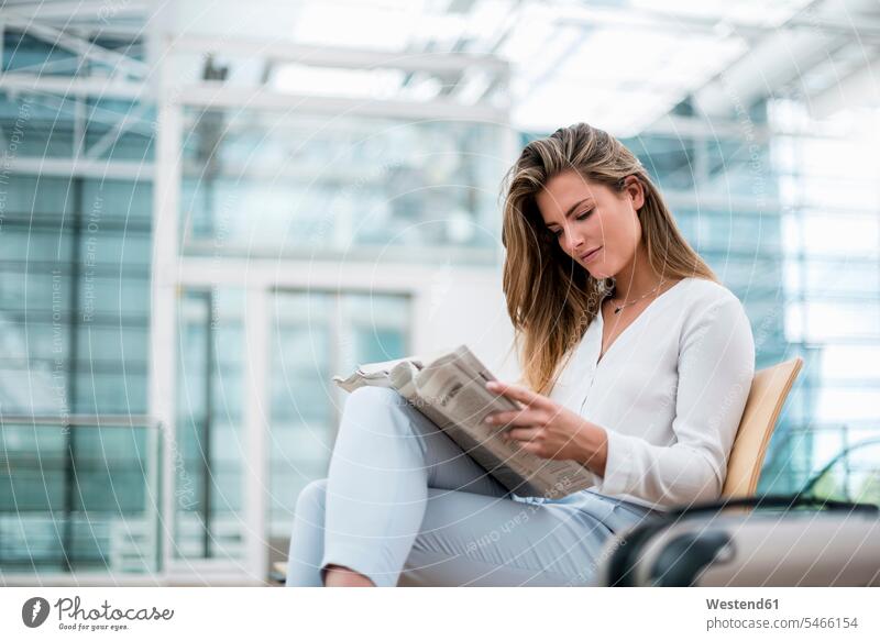 Young businesswoman sitting outdoors with suitcase reading newspaper businesswomen business woman business women newspapers suitcases Seated business people