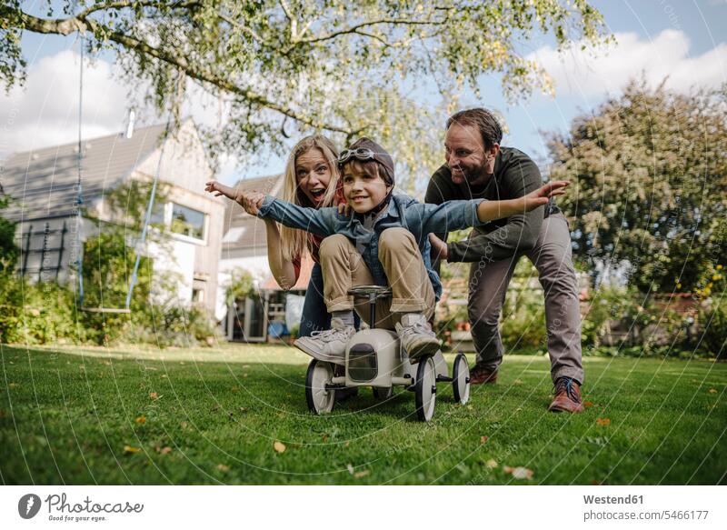 Boy sitting on toy car, pretending to fly, parents encourageing him toys cars toy cars Auto automobile Automobiles motorcar motorcars smile Seated play delight