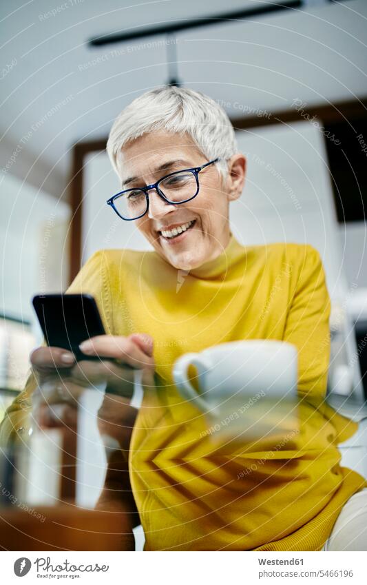 Senior woman drinking coffee, checking text messages on her smartphone human human being human beings humans person persons caucasian appearance