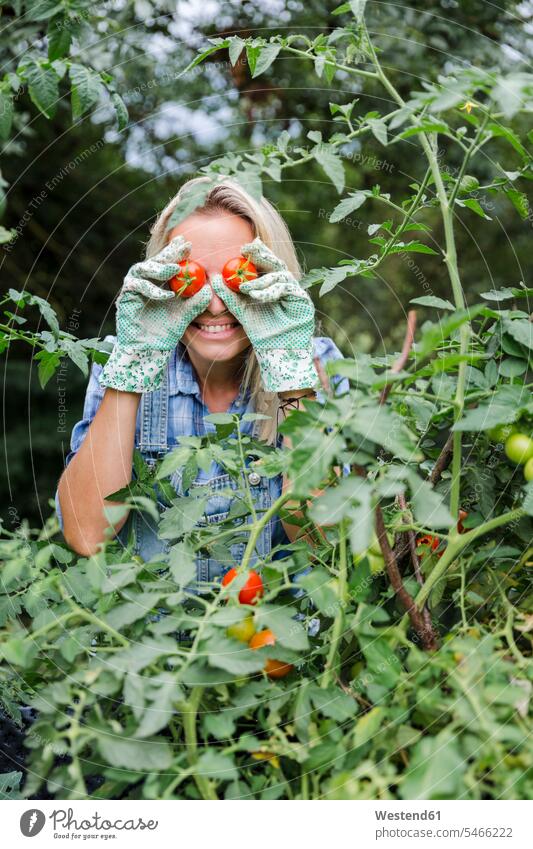 Blond smiling woman harvesting tomatoes, tomatoes on eyes smile delight enjoyment Pleasant pleasure happy Contented Emotion pleased blindness ripeness