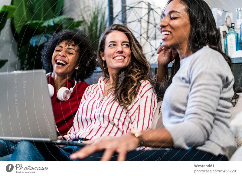 Three happy women with laptop sitting on couch Laptop Computers laptops notebook Seated woman females happiness settee sofa sofas couches settees female friends