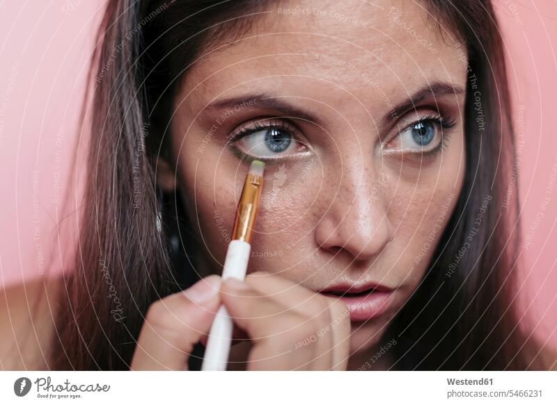 Close up of a young brunette woman with beautiful blue eyes applying eyeshadow with an eye brush studio shot indoor indoors interior shot interiour shots