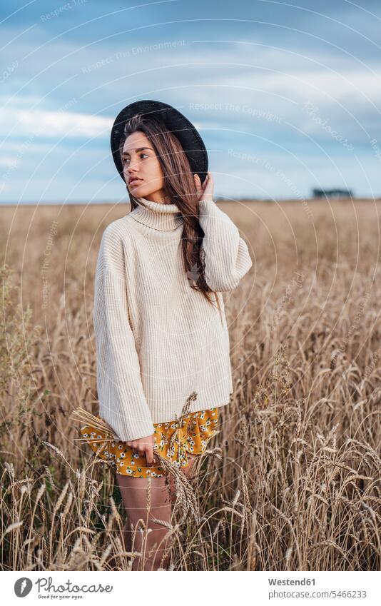 Portrait of young woman wearing hat and oversized turtleneck pullover standing in corn field hats Grain field Cornfield Corn Field Cornfields Corn Fields