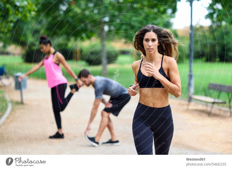 Young athlete running in a park, others stretching in background exercising exercise training practising jogger joggers female jogger parks Fitness fit Jogging