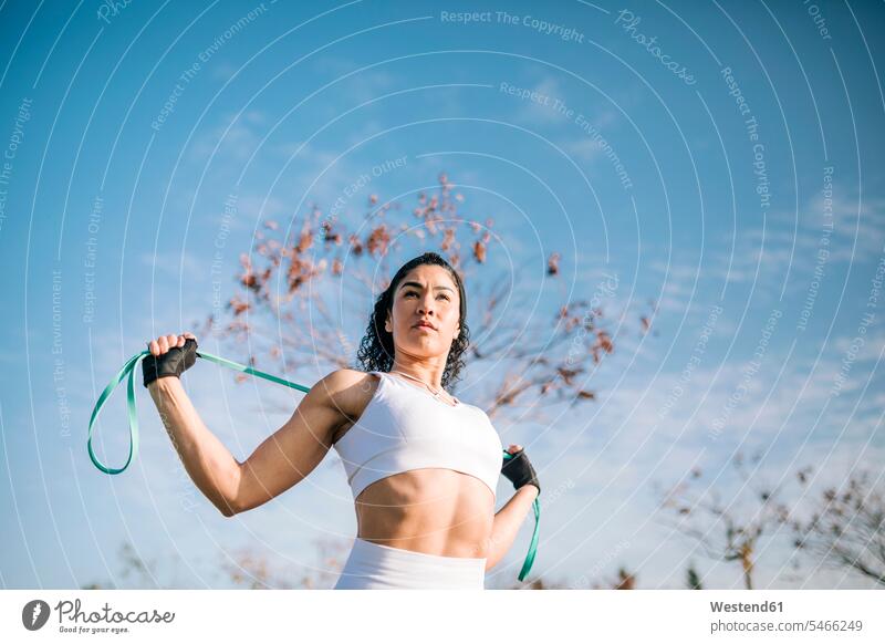 Confident sportswoman with resistance band against sky on sunny day color image colour image outdoors location shots outdoor shot outdoor shots daylight shot