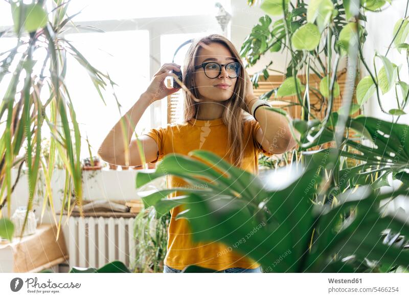 Young woman surrounded by plants listening to music with headphones windows T- Shirt t-shirts tee-shirt headset Eye Glasses Eyeglasses specs spectacles hear