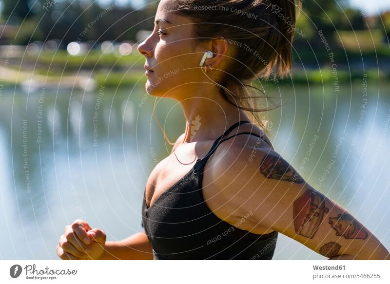 Tattooed young woman with earbuds jogging at the riverside exercise practising train training hear run seasons summer time summertime summery colour colours