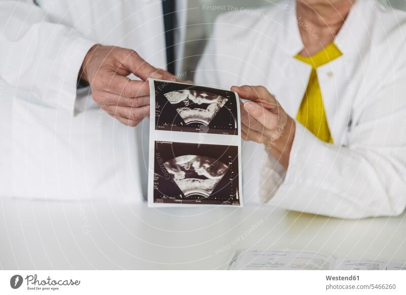Two doctors holding ultrasound images of fetus Occupation Work job jobs profession professional occupation Tables desks health healthcare